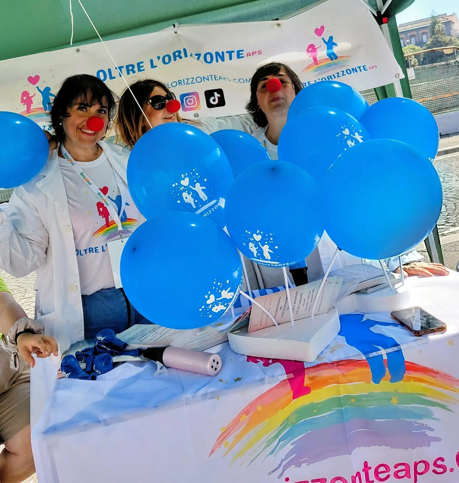 Volontarie con nasi rossi e palloncini celesti al gazebo dell’associazione